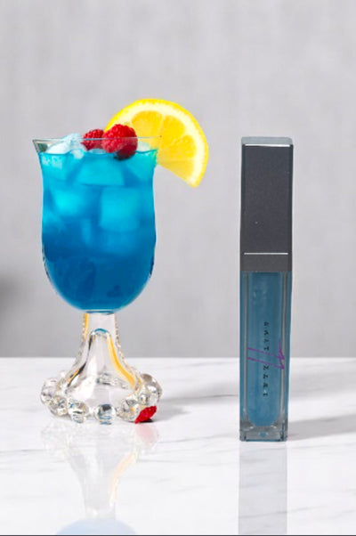 Blue Raspberry lip gloss in sleek container with a fruity drink beside it.